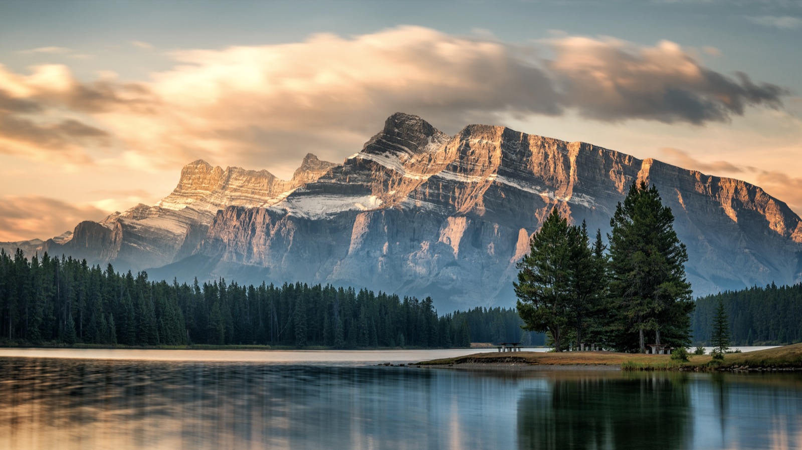 Mount Rundle in Banff National Park at sunrise, with a lake and evergreen forest in the foreground
